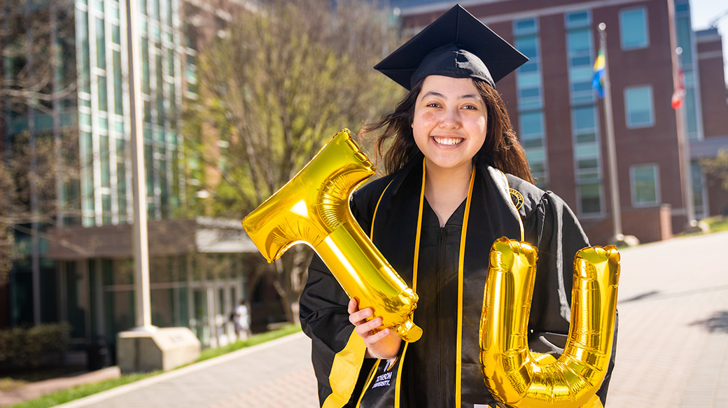 TU Student in graduation cap and gown holding a gold TU balloon