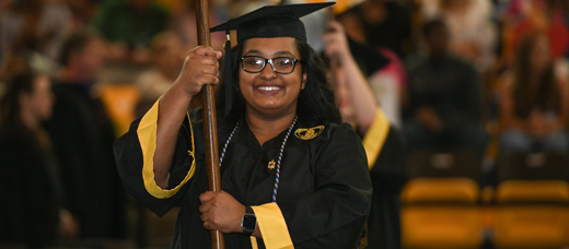 Towson graduating student walking with a department flag